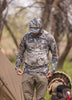 Close-up of a person wearing a camouflage hunting hoodie and cap, adjusting gear outdoors.